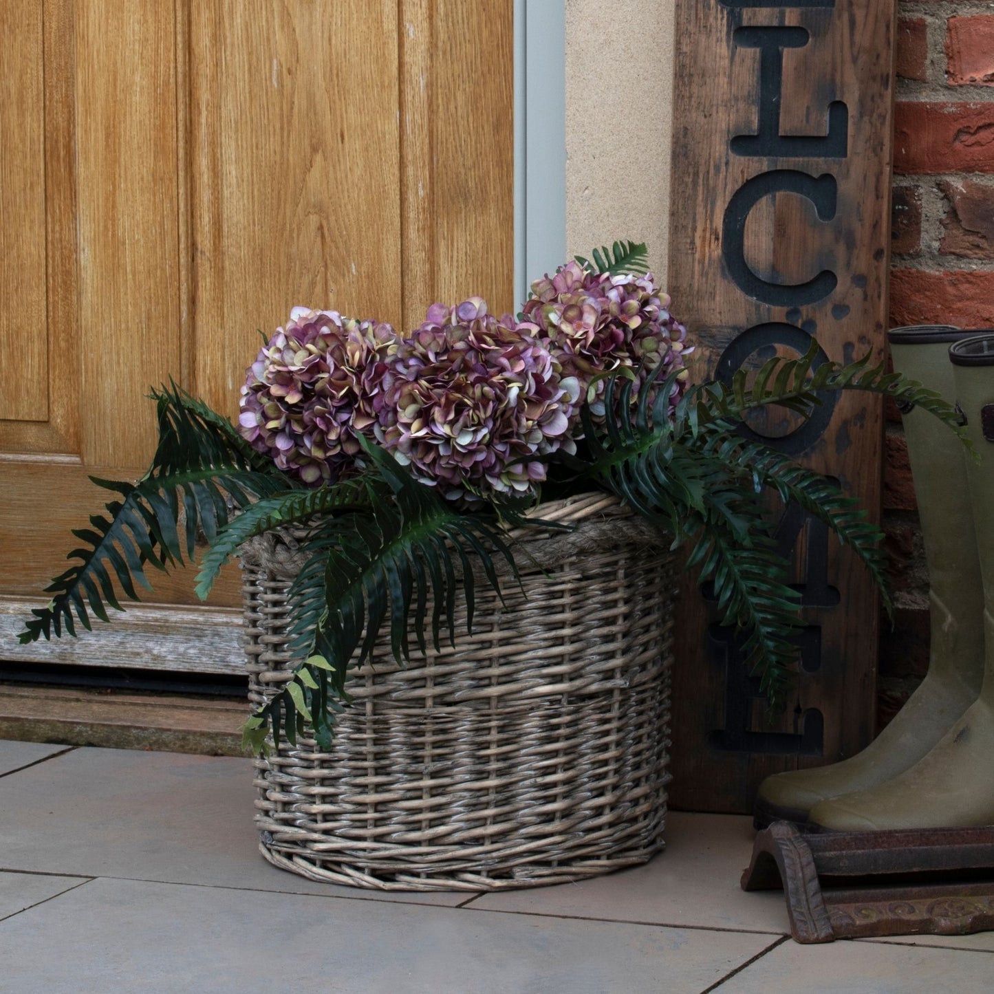 Wicker basket with flowers in front of a wooden door and 'Welcome' sign.