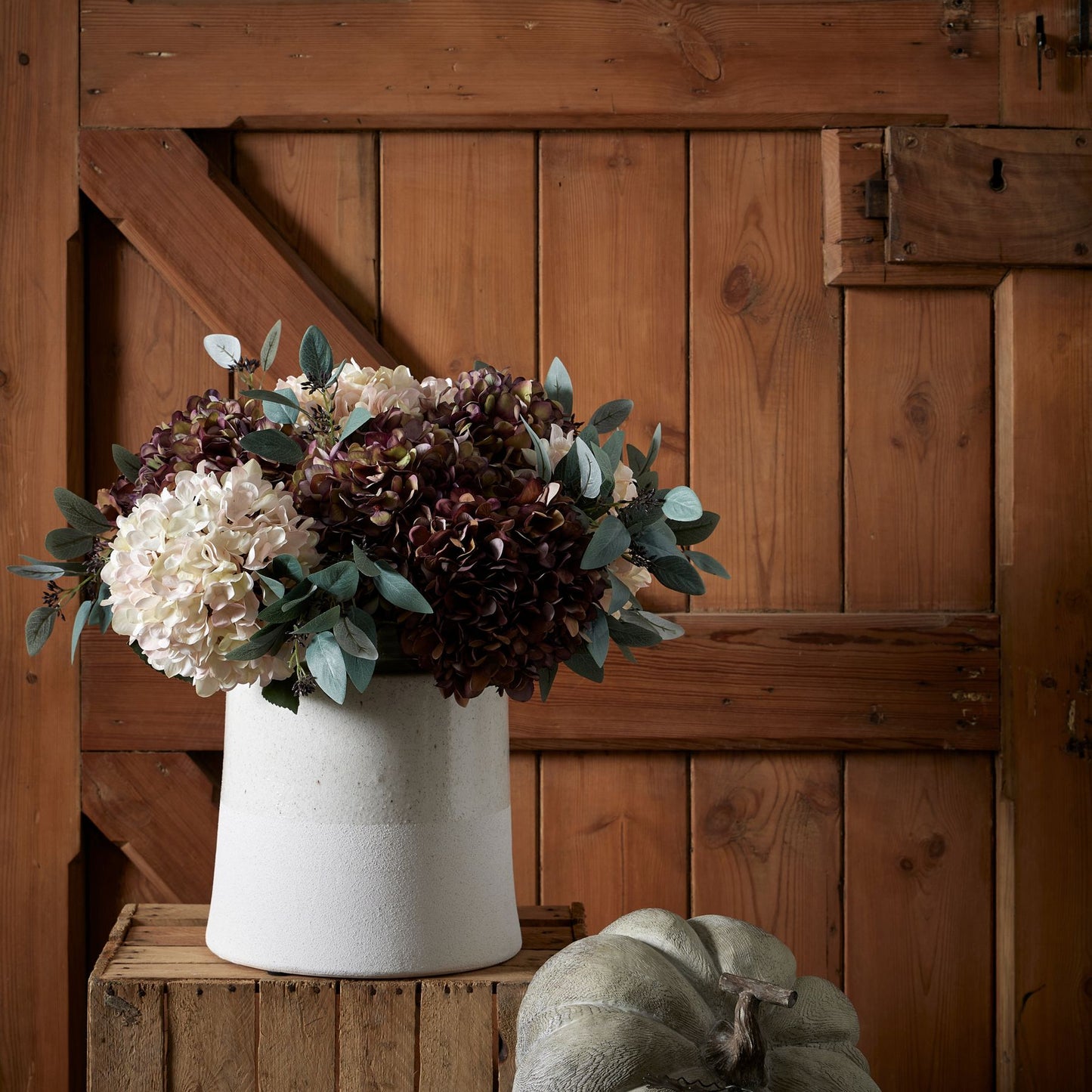 Floral arrangement in a white vase on a wooden surface with a wooden background