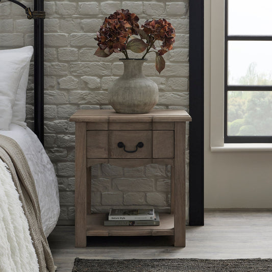 Wooden nightstand with a vase of flowers next to a bed in a bedroom.