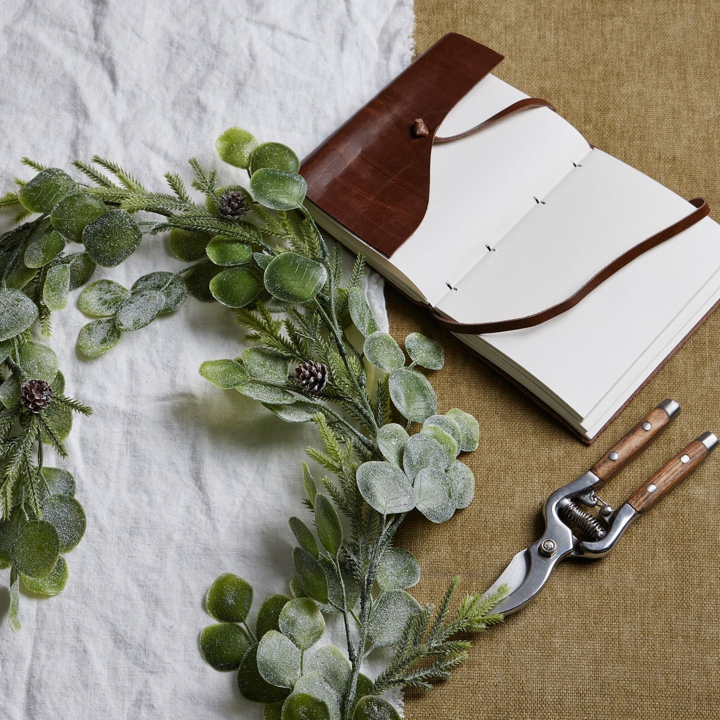 Open notebook with a brown leather cover, greenery, and pruning shears on a textured surface.