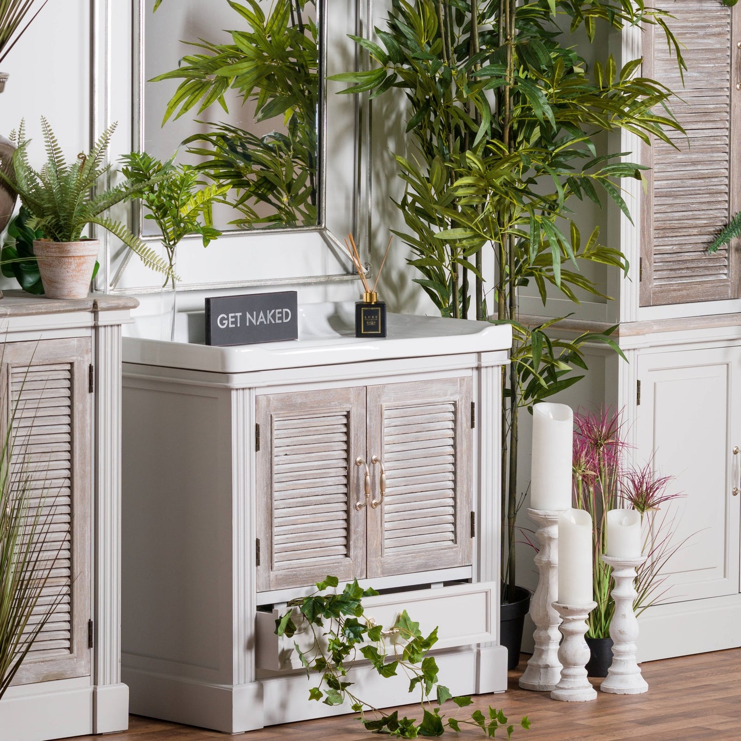 White bathroom vanity with wooden shutters, decorative plants, and candles.