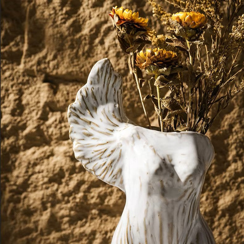 Decorative vase shaped like a woman's torso with dried sunflowers against a textured wall.