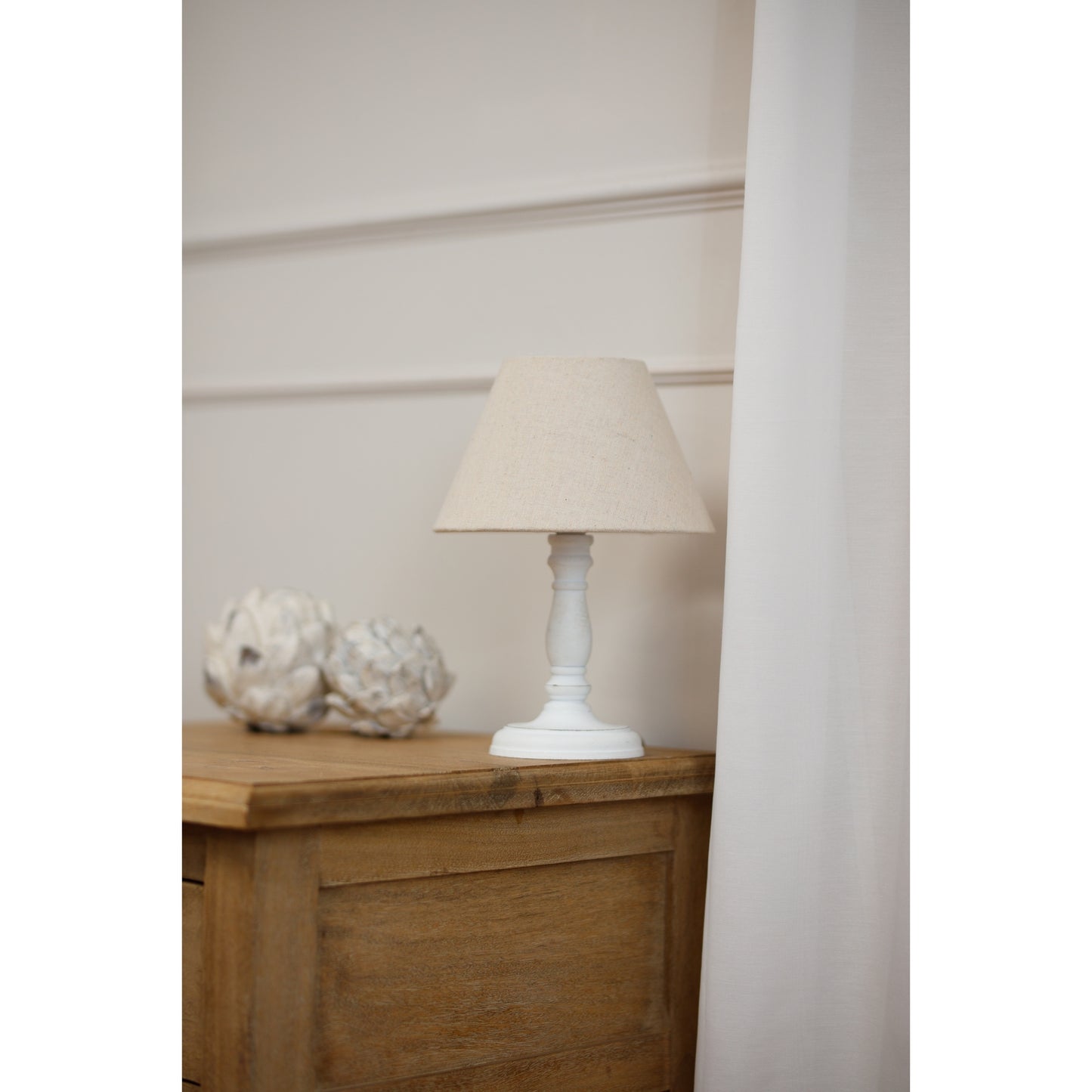 Table lamp with a beige shade on a wooden side table against a white wall.