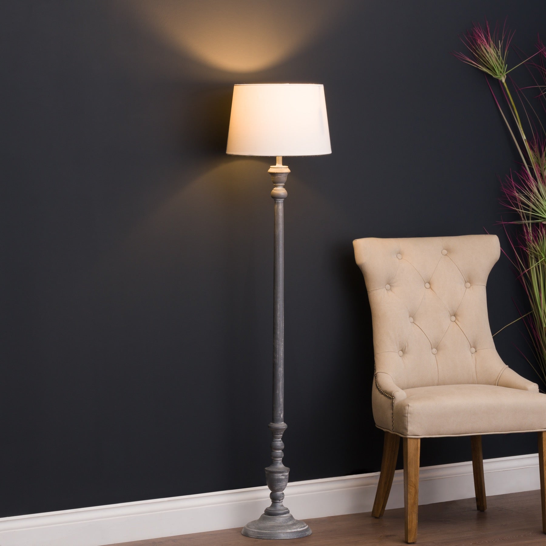 Floor lamp next to a beige chair against a dark wall