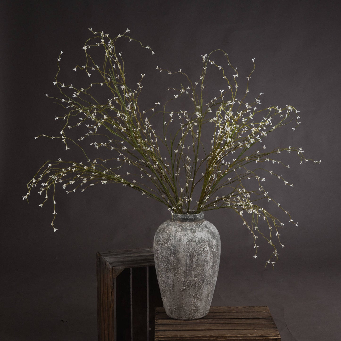 Decorative plant arrangement in a textured vase on a wooden surface with a dark background