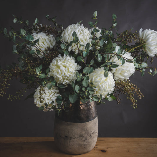 Bouquet of white flowers with green leaves in a rustic vase on a wooden surface.