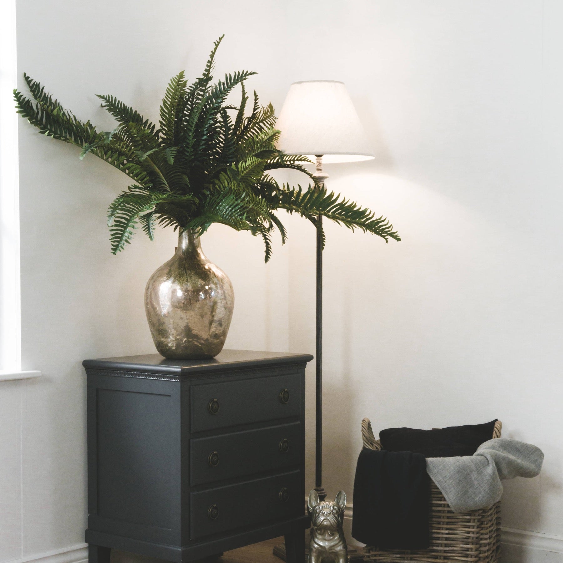 Vase with green plant on a dark wooden cabinet next to a lamp and wicker basket.