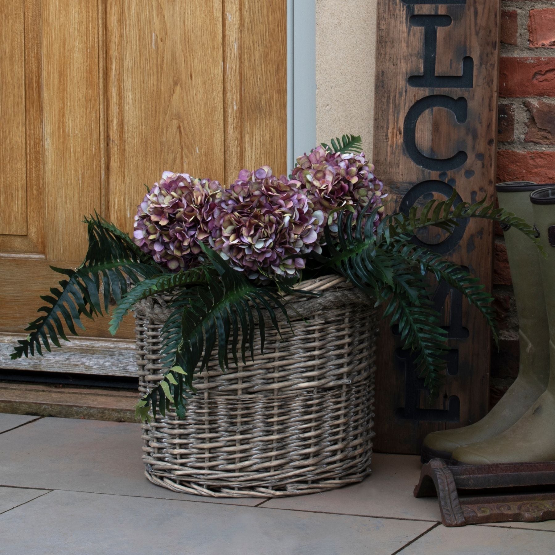 Wicker basket with flowers in front of a wooden door and 'Welcome' sign.