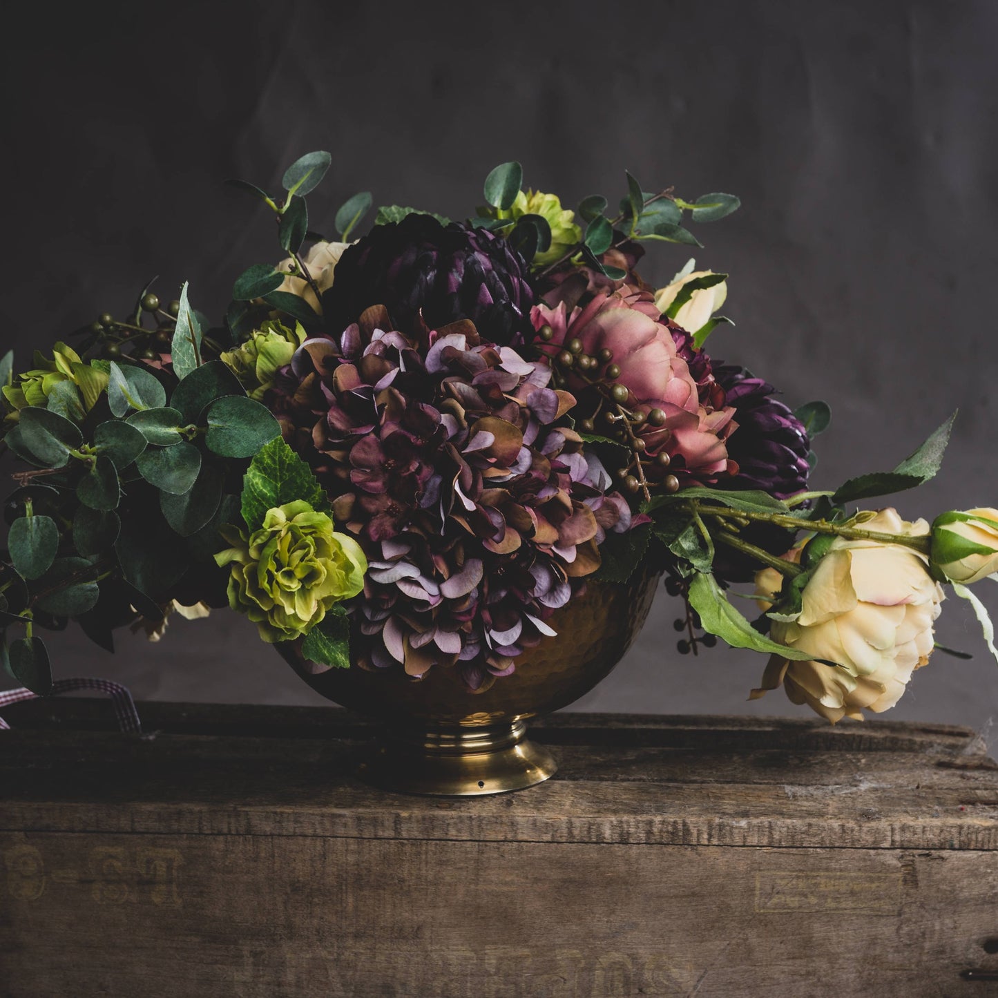 Floral arrangement in a brass vase on a wooden surface with a dark background