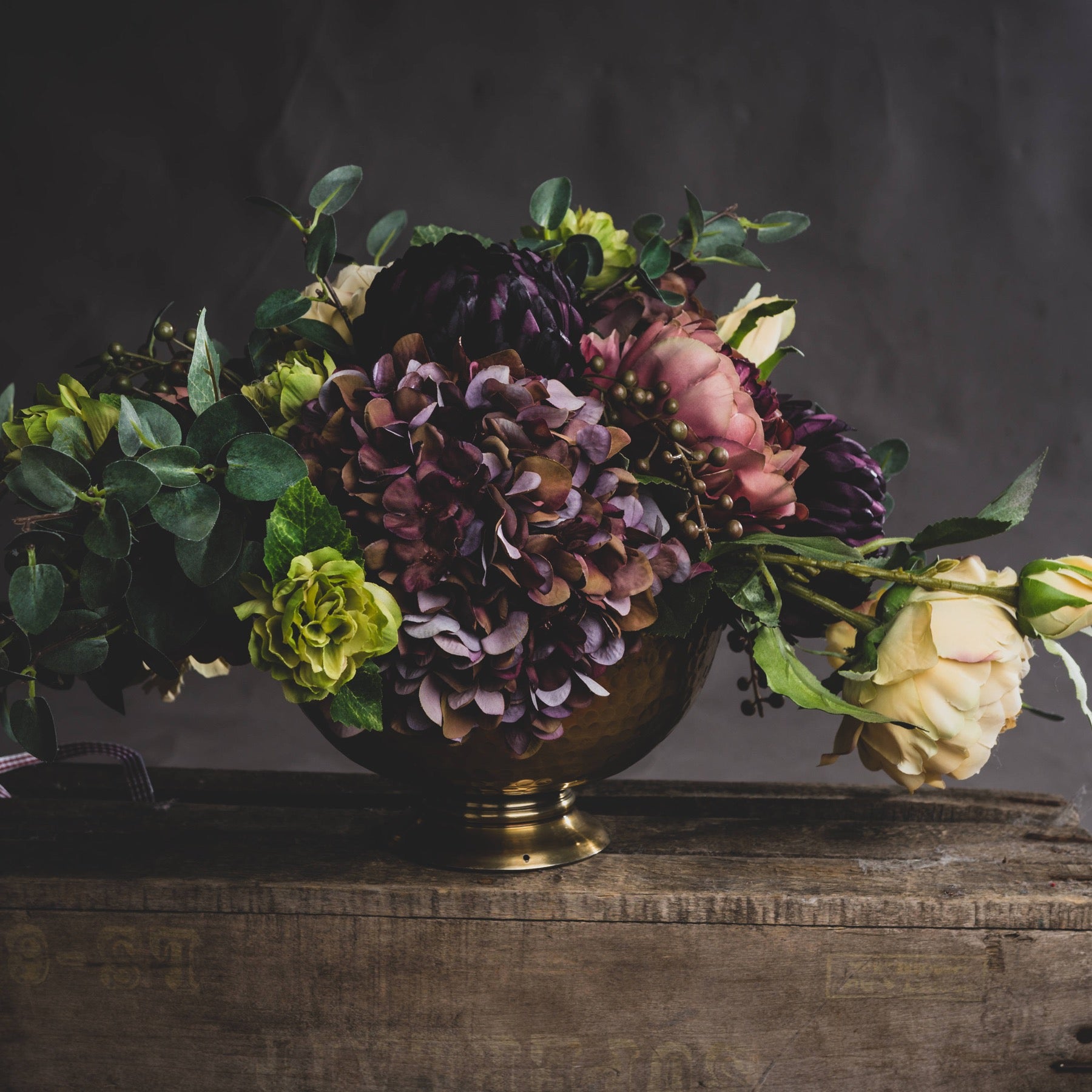 Floral arrangement in a brass vase on a wooden surface with a dark background