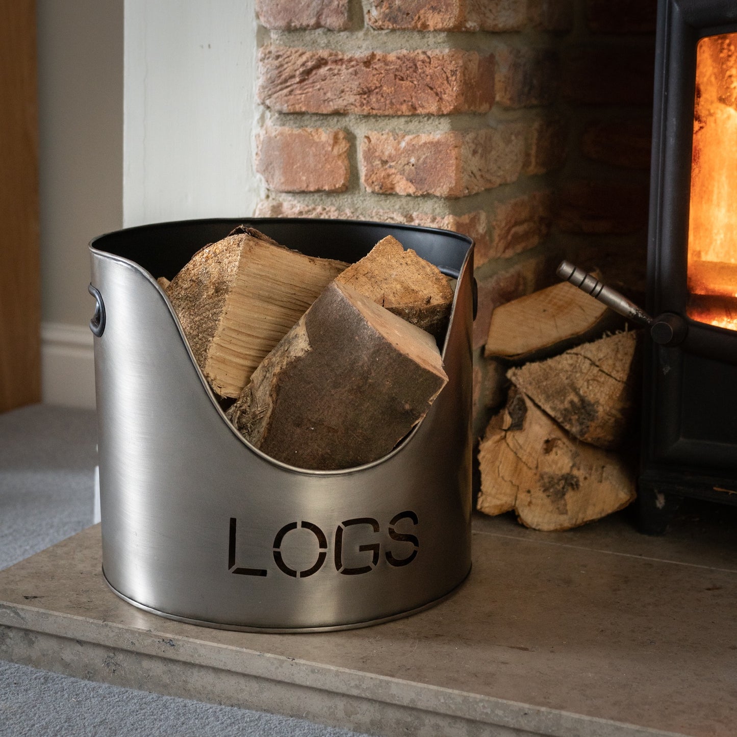 Metal log holder with 'LOGS' engraving in front of a fireplace.