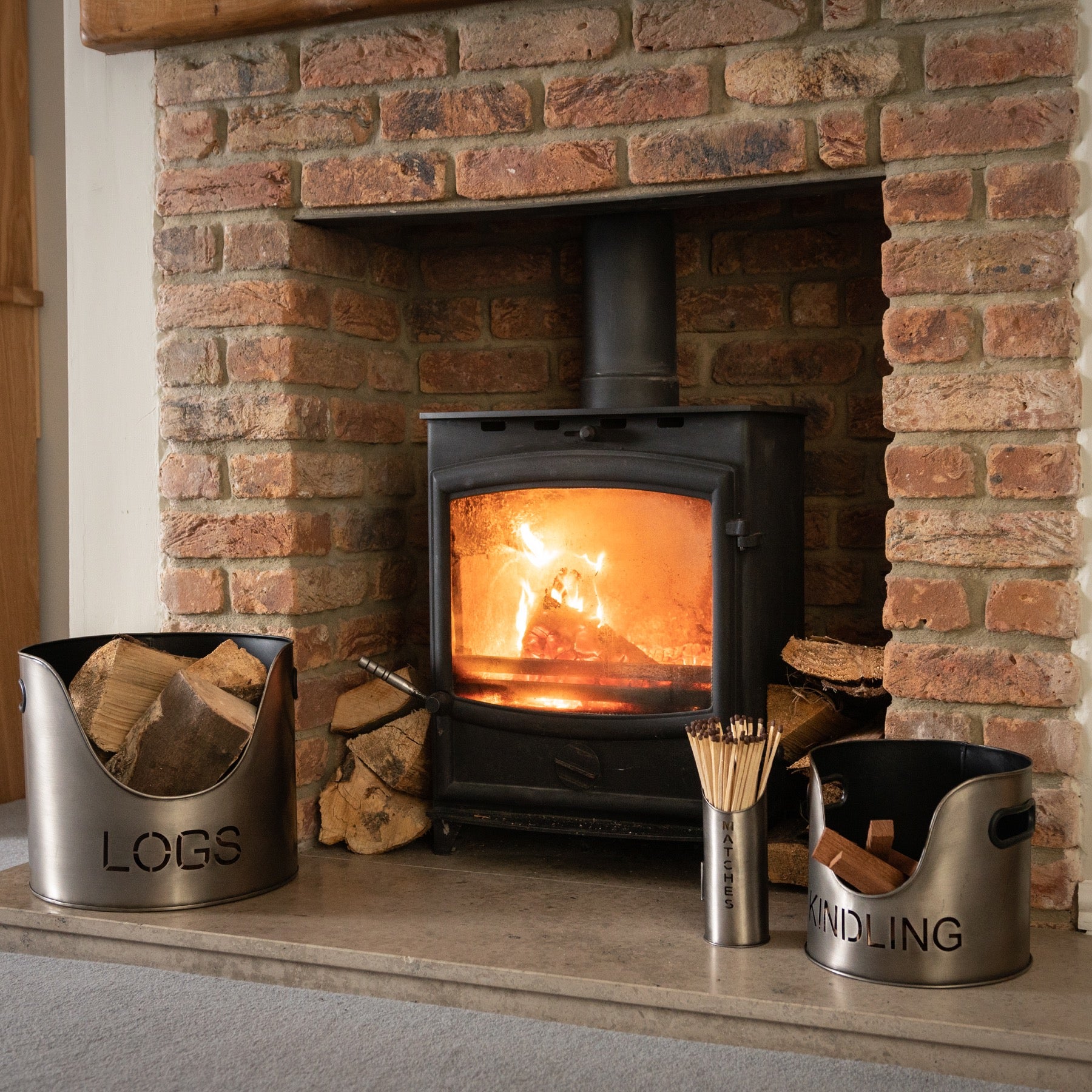 Brick fireplace with a lit fire, logs on the left, and kindling on the right.