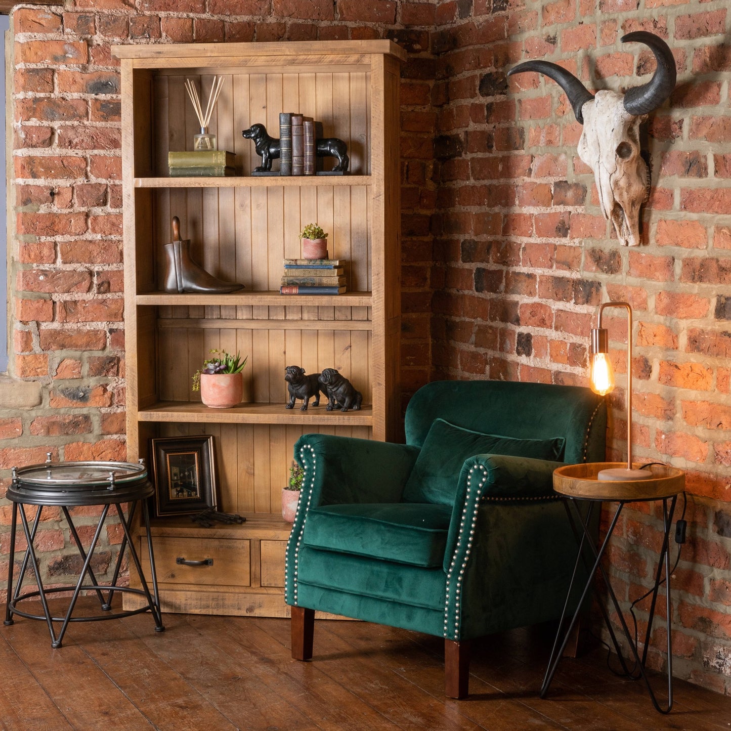 Green armchair in a room with wooden bookshelf and brick wall