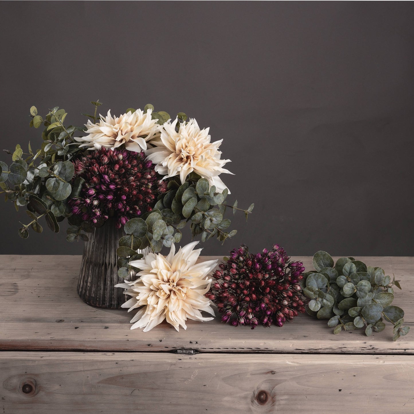 Floral arrangement with beige and purple flowers on a wooden surface against a dark background