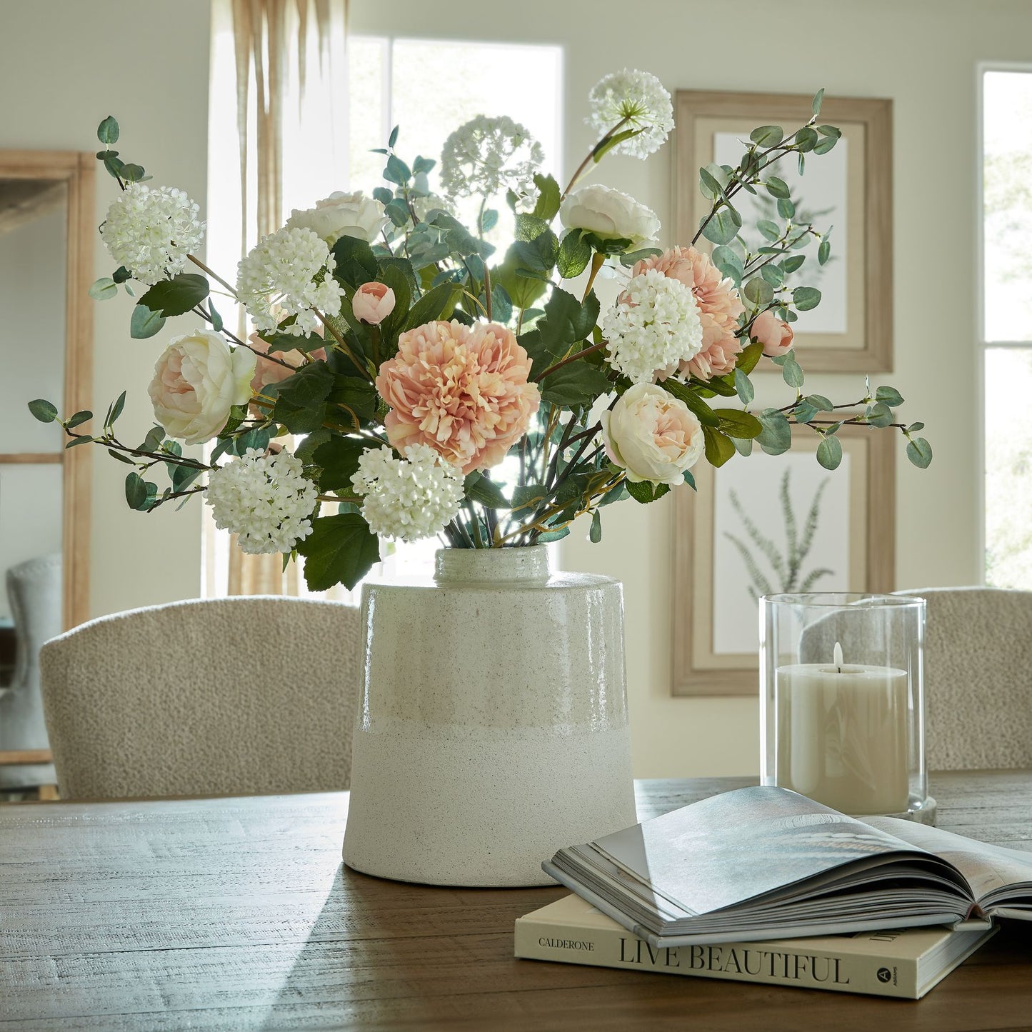Floral arrangement in a vase on a table with a candle and book in the background.