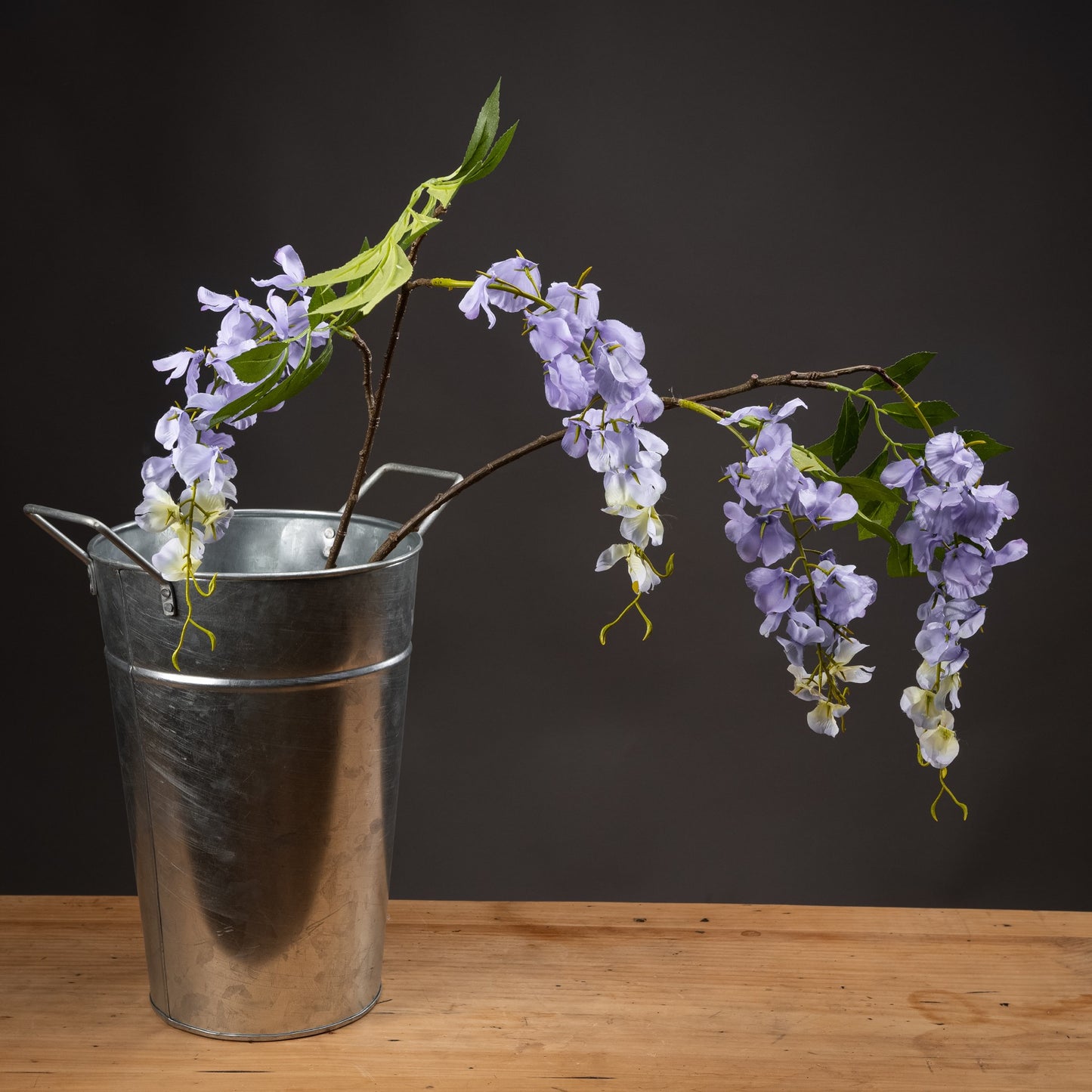 Metal bucket with purple flowers on a wooden surface against a dark background