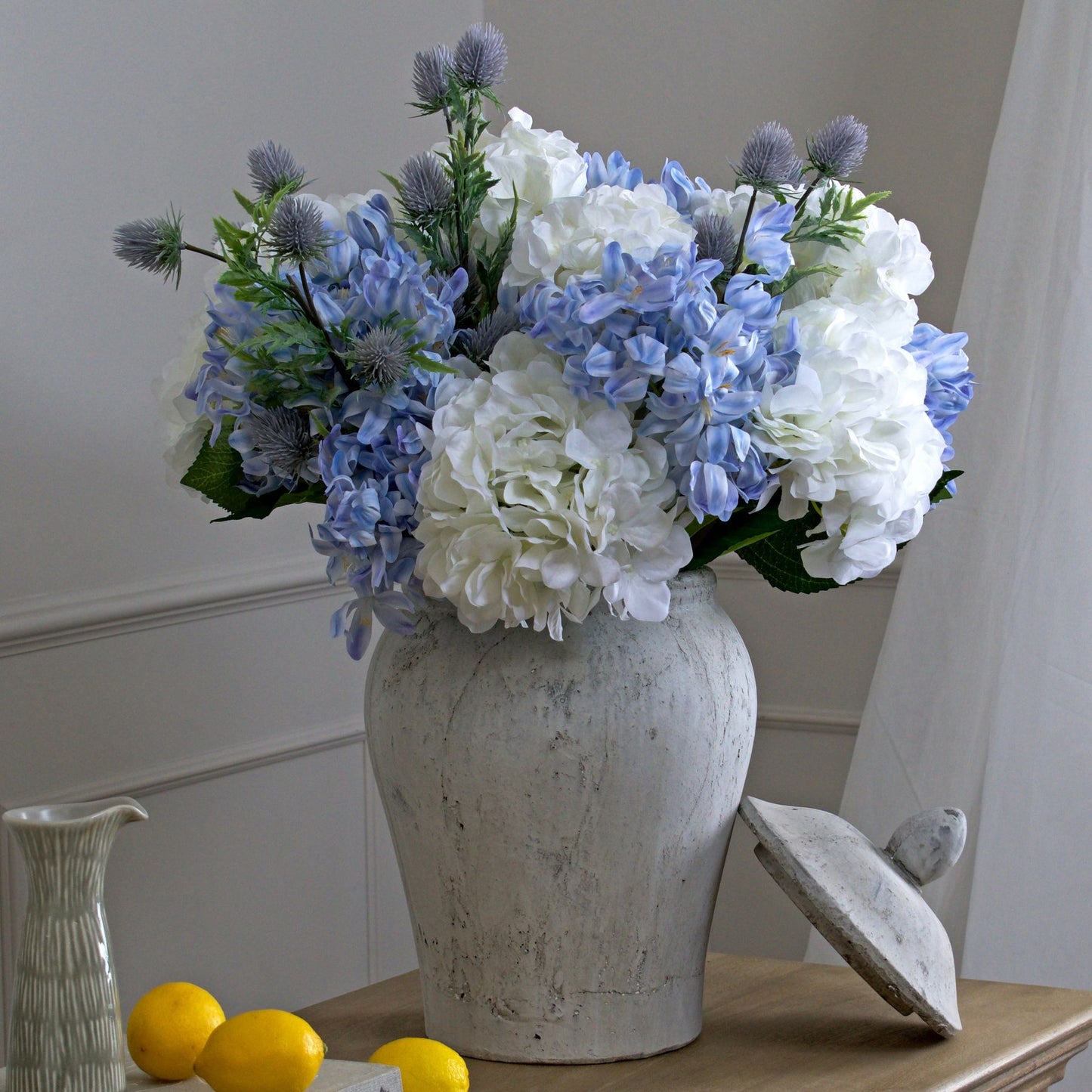 Vase with blue and white flowers on a wooden surface with lemons and a decorative object.