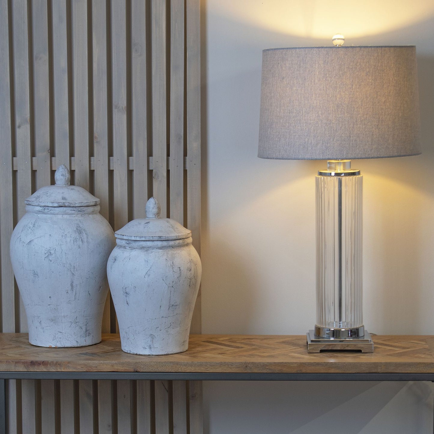Two white ceramic jars and a tall lamp on a wooden surface with a neutral background