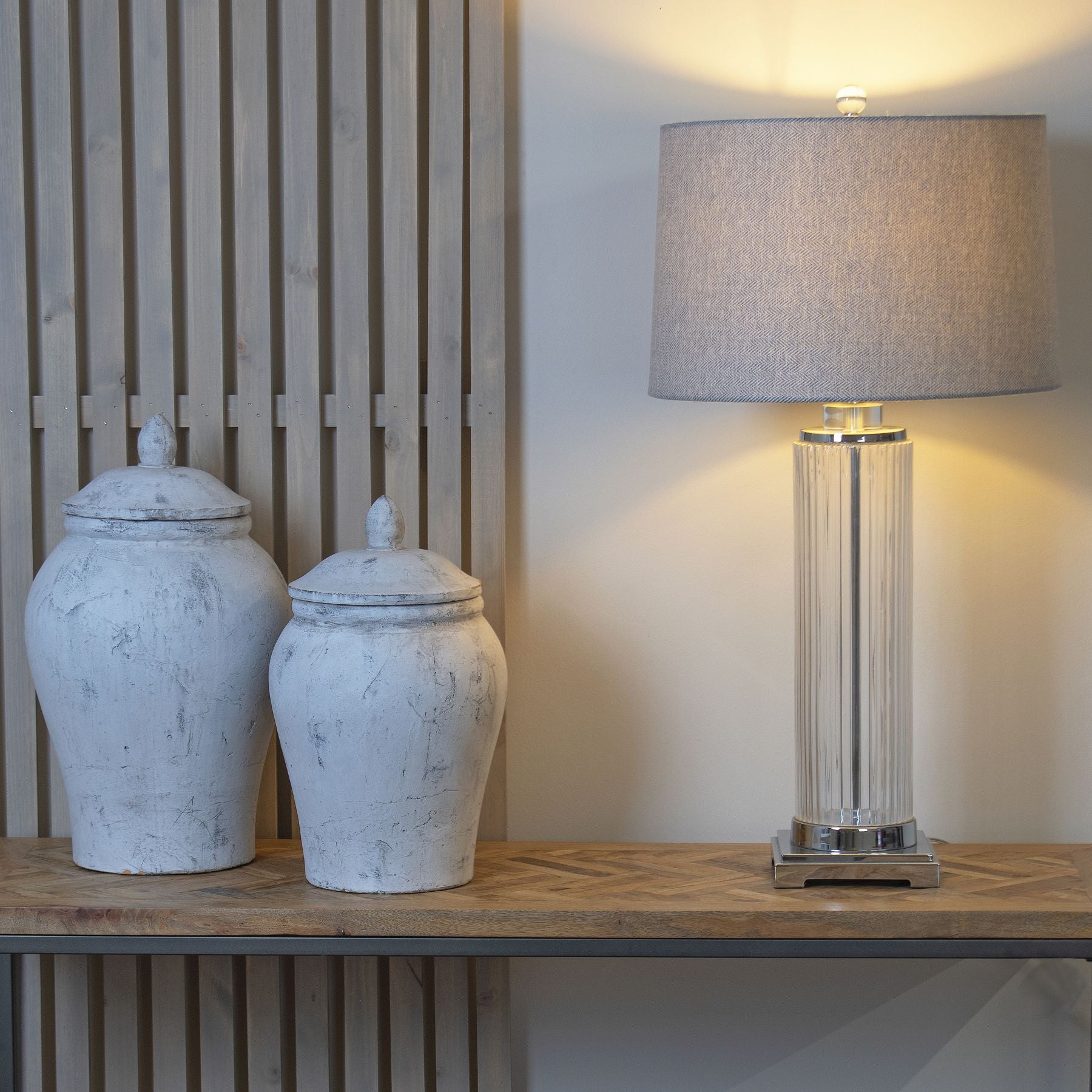 Two white ceramic jars and a tall lamp on a wooden surface with a neutral background