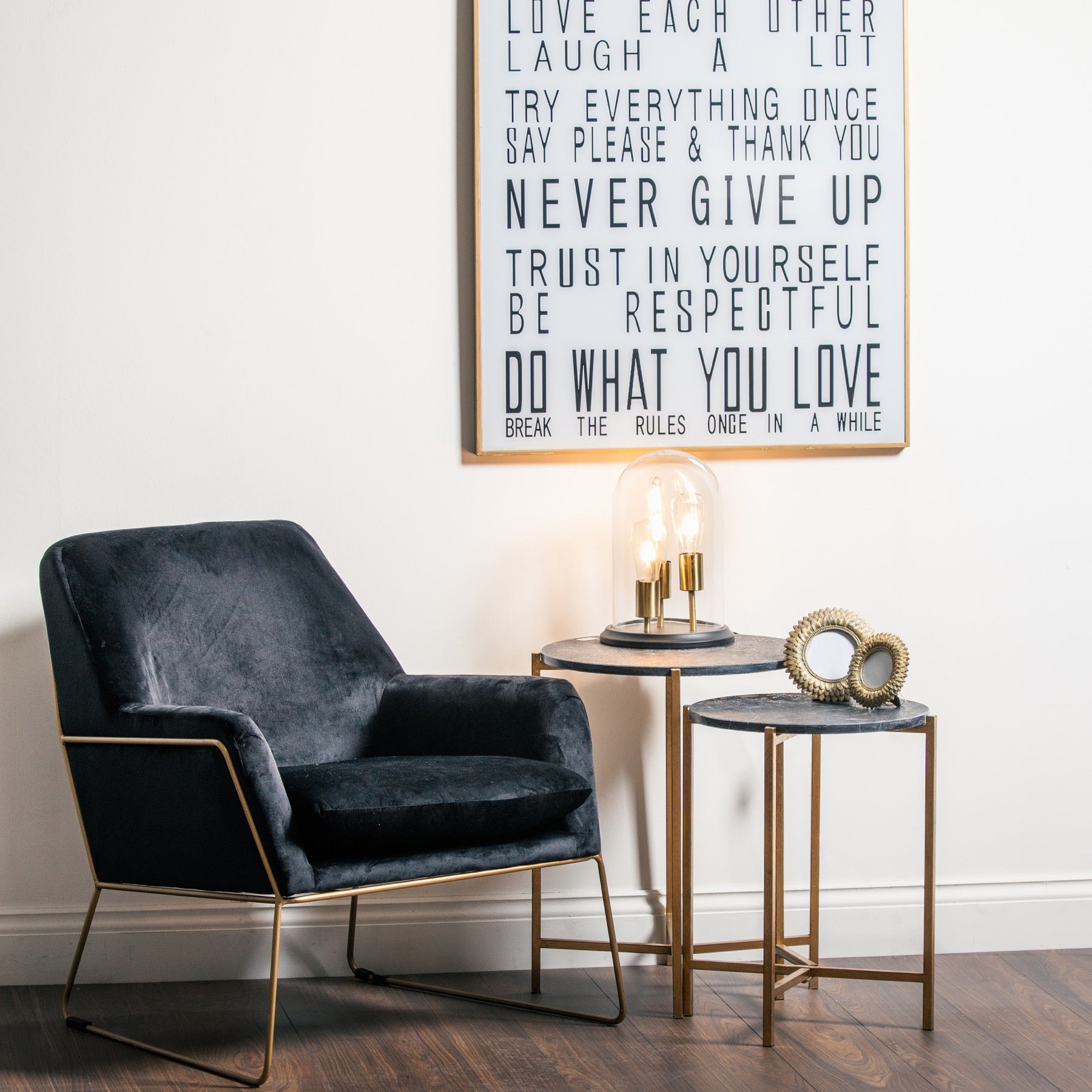 Modern interior with a dark gray armchair, side tables, and a motivational poster on the wall.