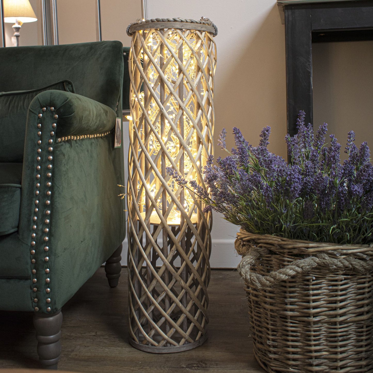 Woven floor lamp next to a green sofa and potted lavender plant in a room.