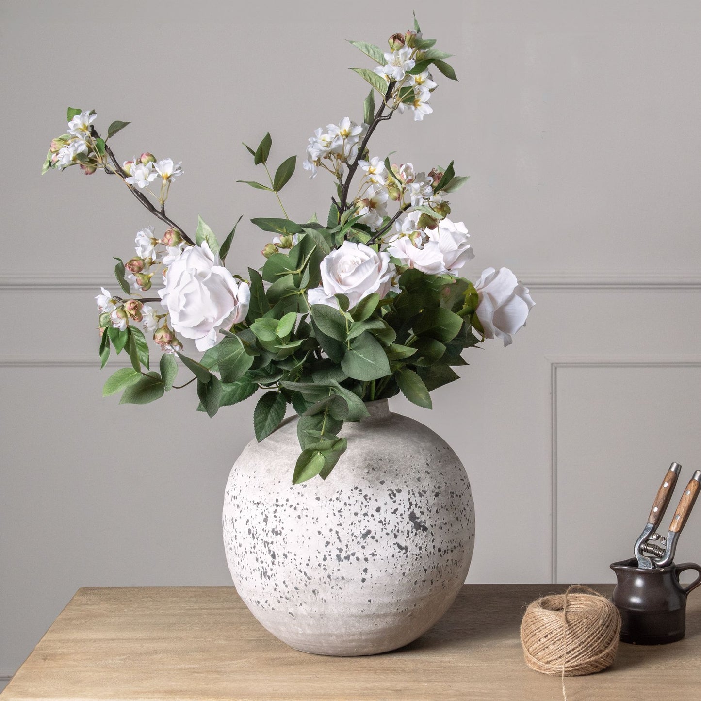 Decorative vase with flowers on a wooden surface against a gray wall