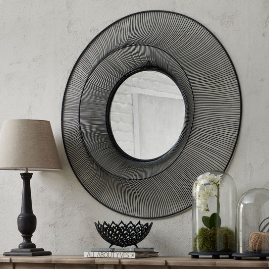 Decorative wall mirror with concentric circles on a neutral wall with a lamp and decorative items below.