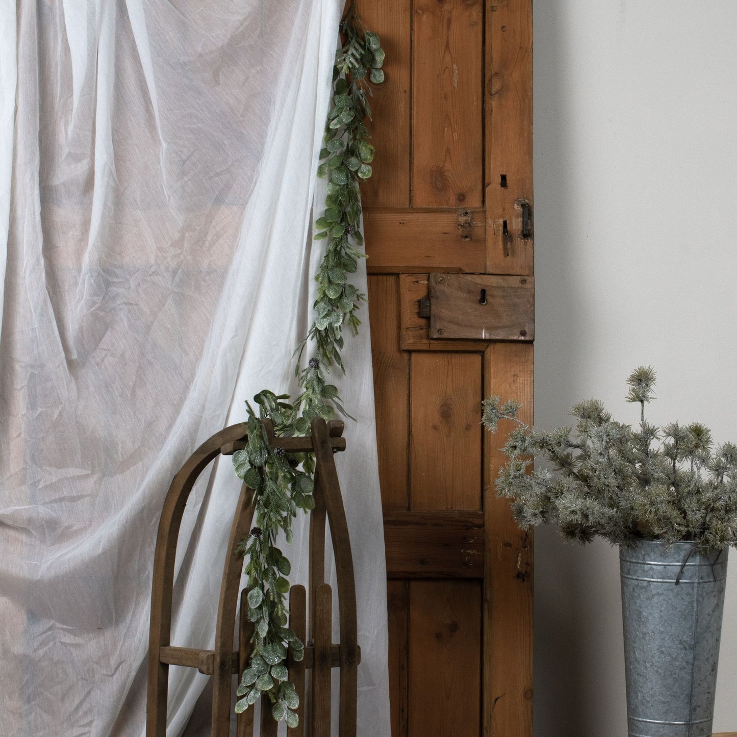 Decorative setup with a wooden chair, draped fabric, and potted plants against a white wall.