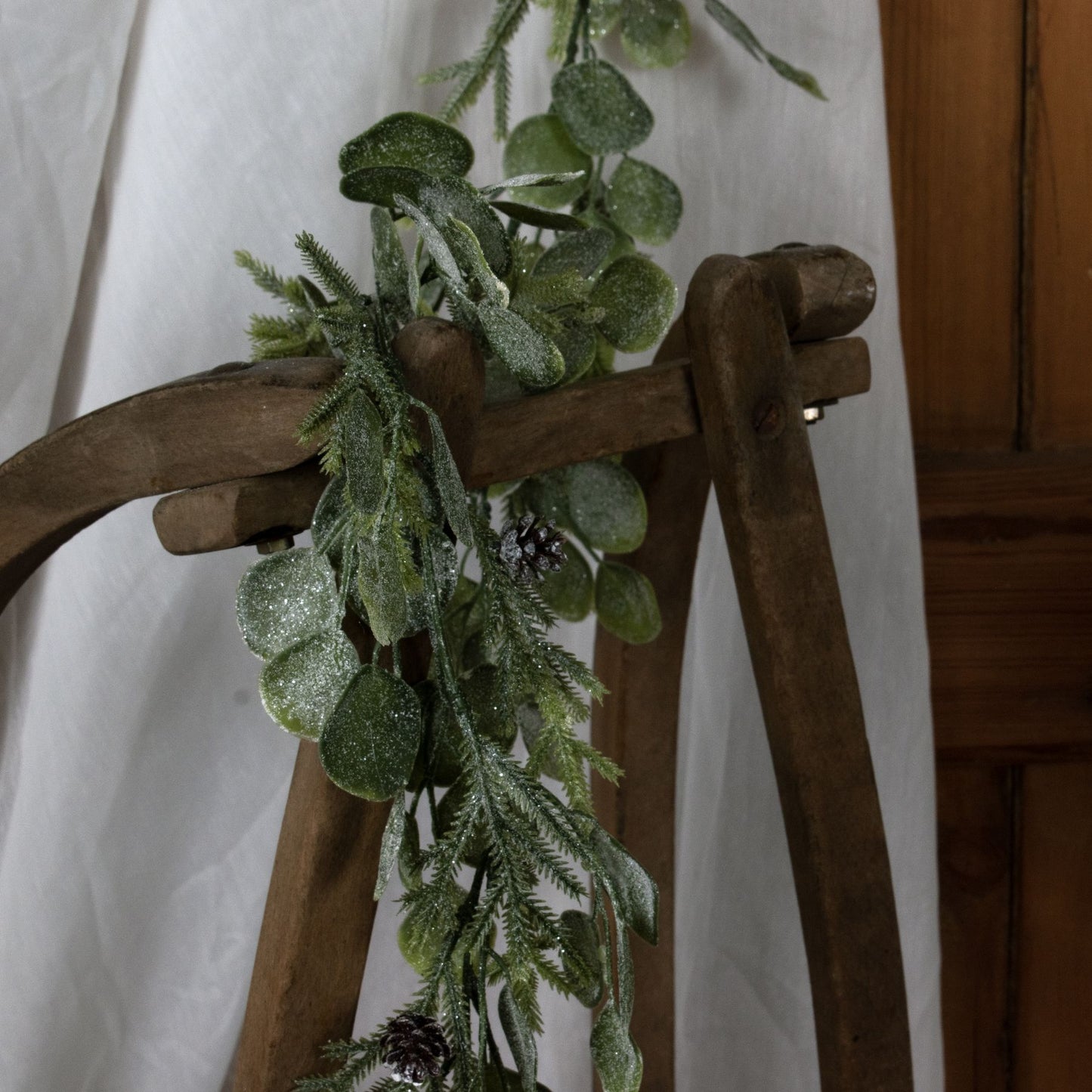 Green leafy garland draped over a wooden chair against a white curtain background