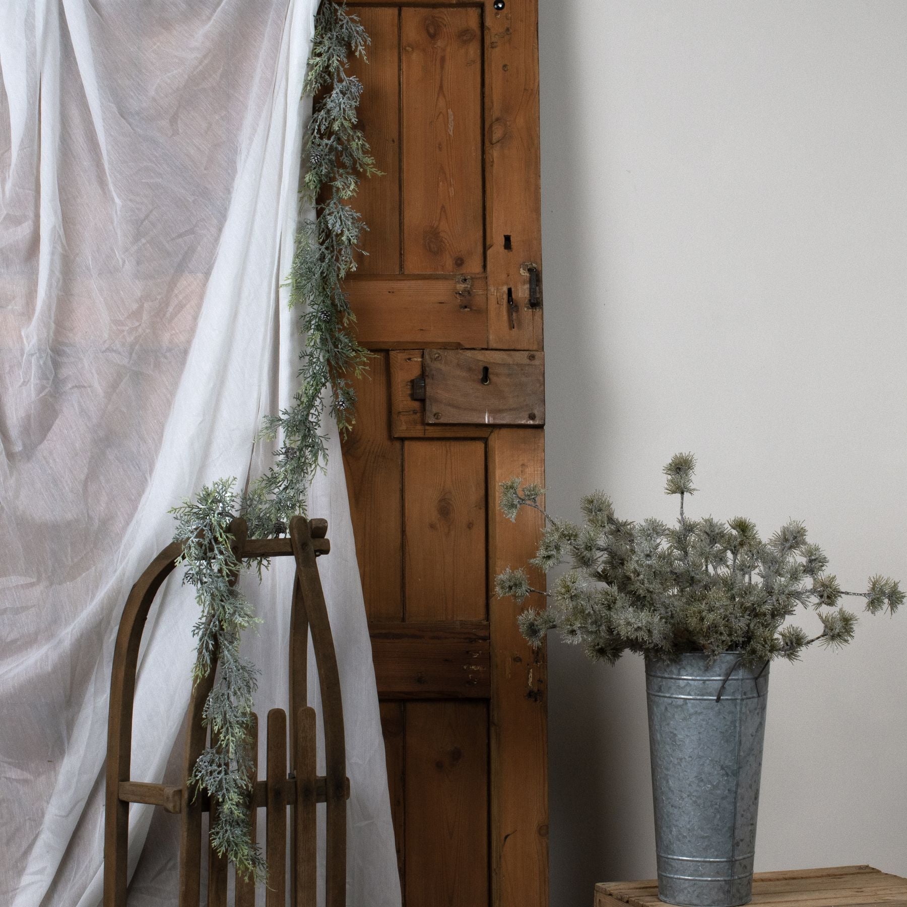 Wooden door with decorative greenery, wooden sled, and metal bucket with plants on a white background