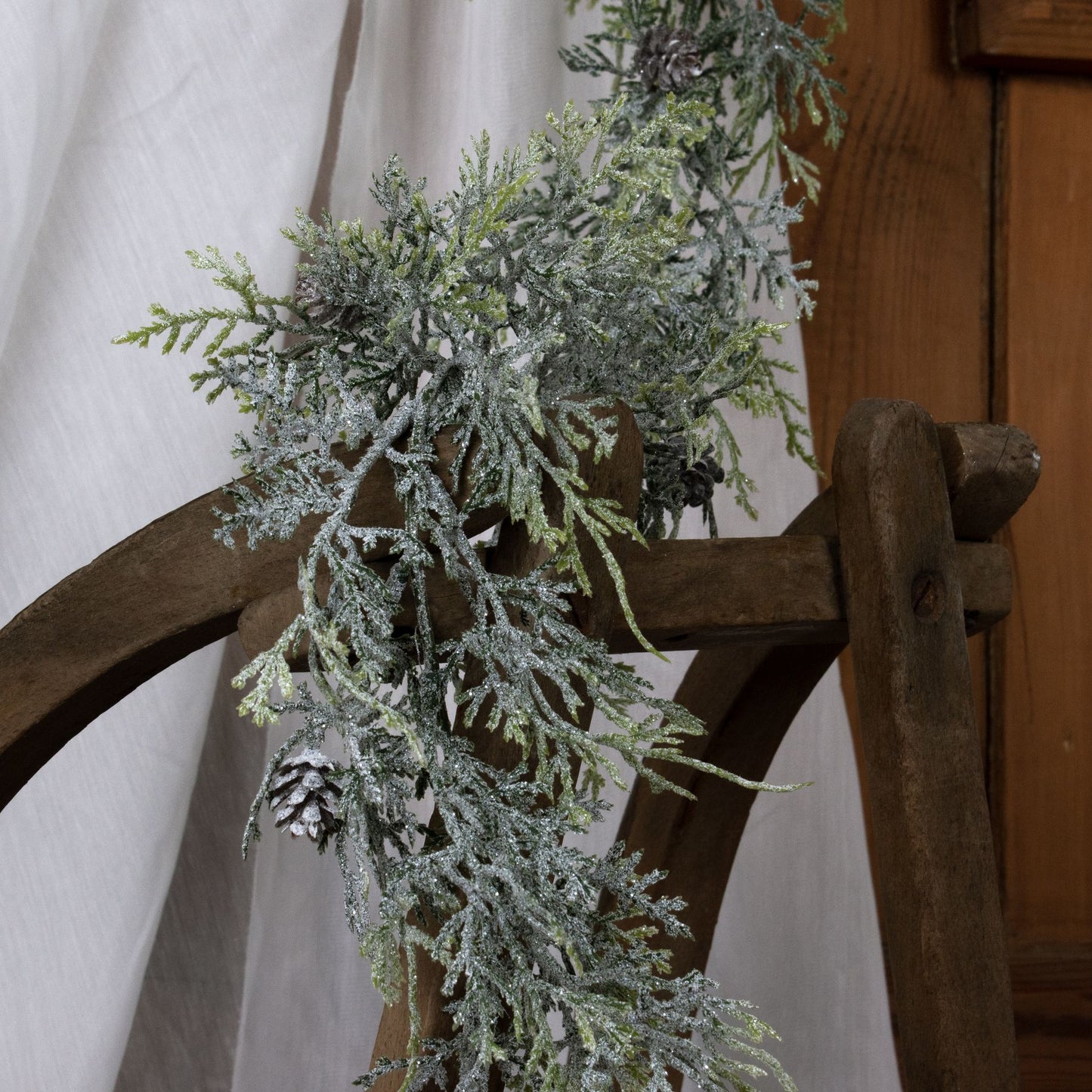 Frosted greenery garland on a wooden chair with a neutral background