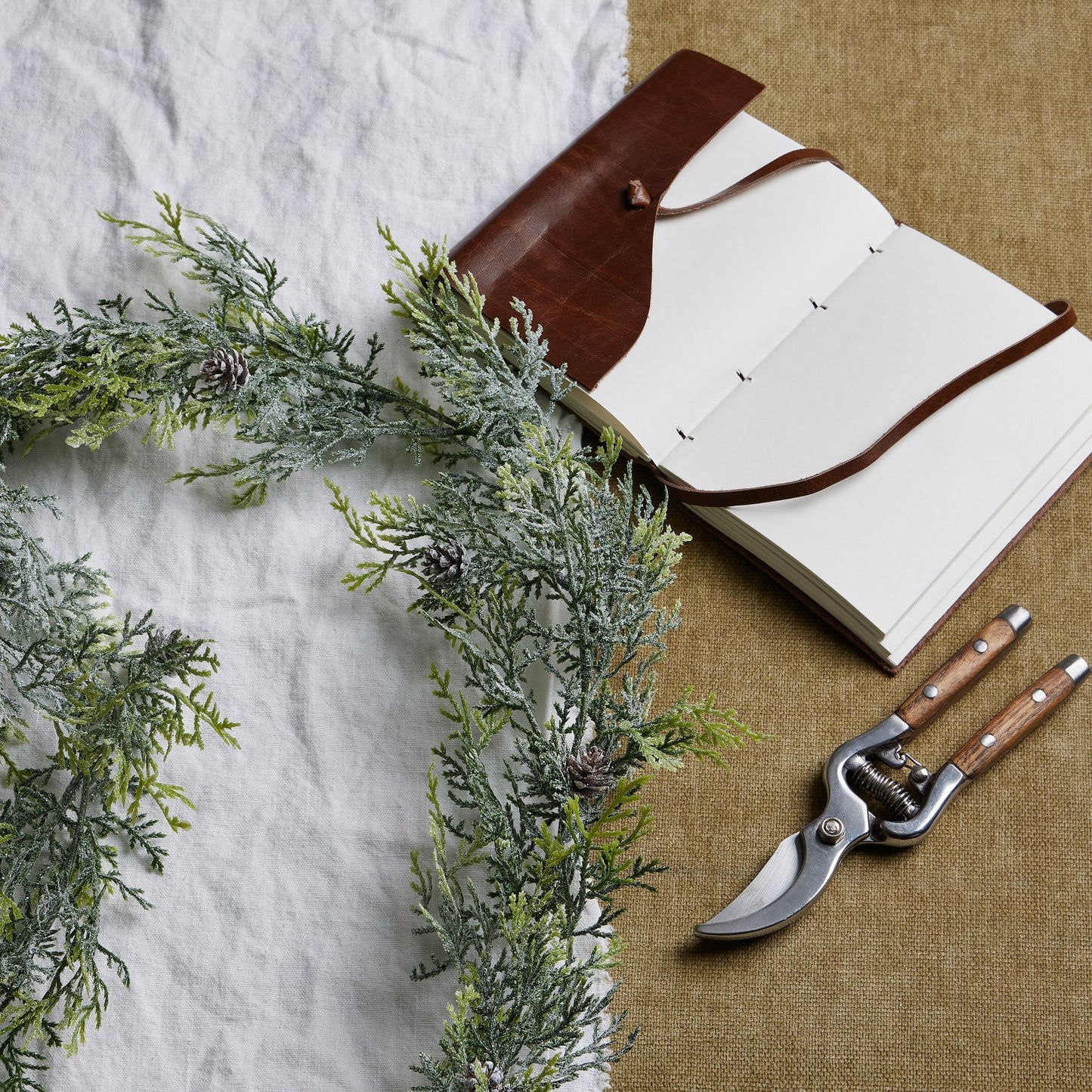 Open notebook with brown leather binding, greenery, and pruning shears on a textured surface