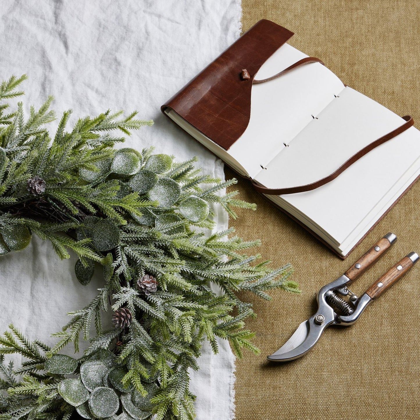 Open notebook with brown leather cover, greenery, and pruning shears on a textured surface