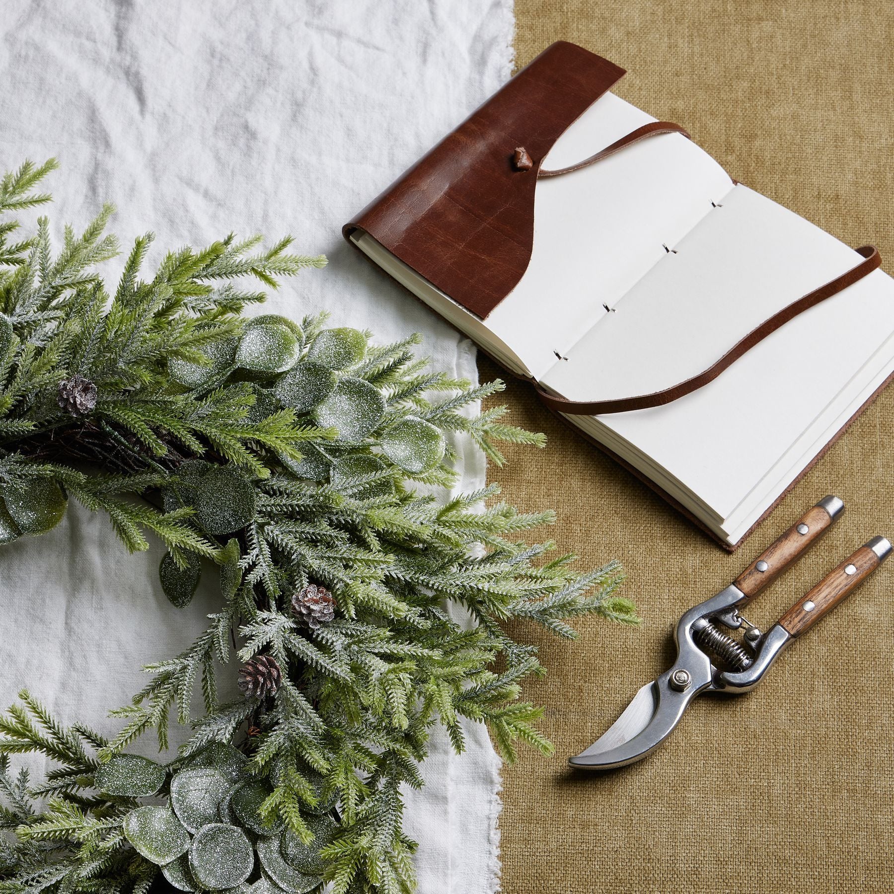 Open notebook with brown leather cover, greenery, and pruning shears on a textured surface