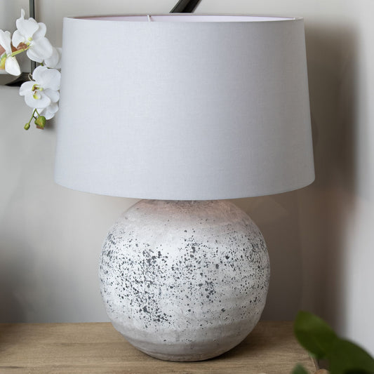 Table lamp with a textured base and white shade on a wooden surface.