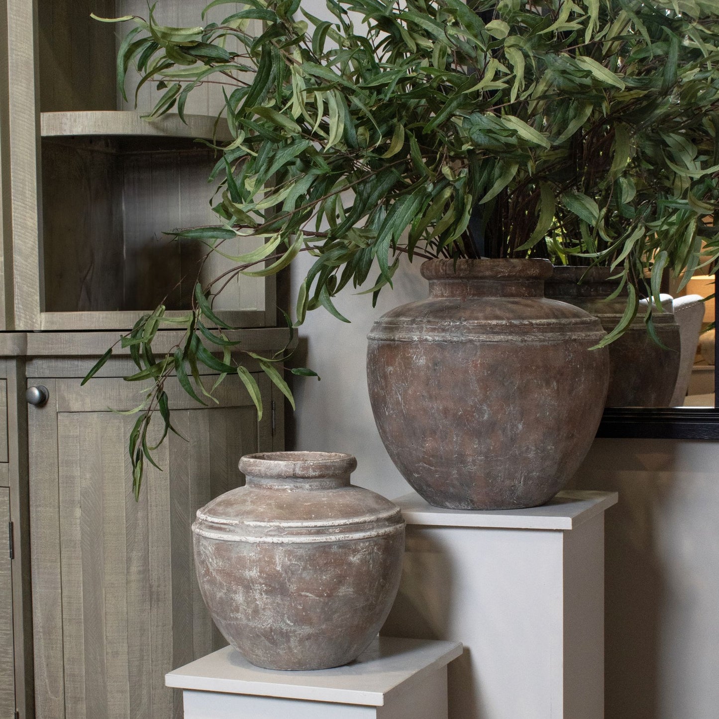 Decorative stone urns with greenery on a white surface next to a wooden cabinet.