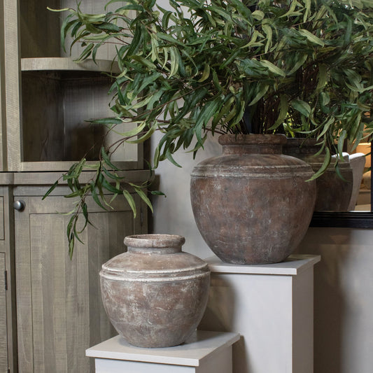 Decorative stone urns with greenery on a white surface next to a wooden cabinet.