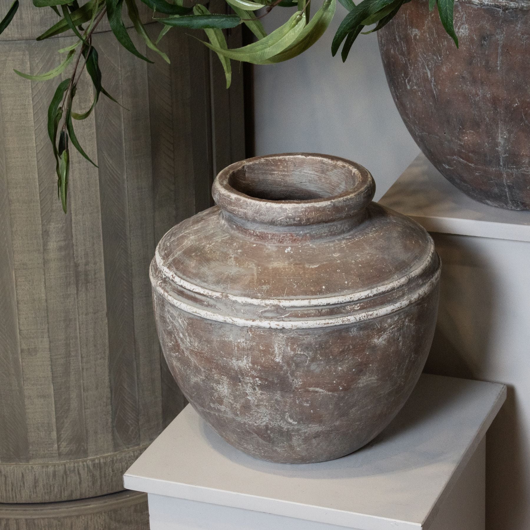 Decorative brown vase on a white surface with a plant in the background