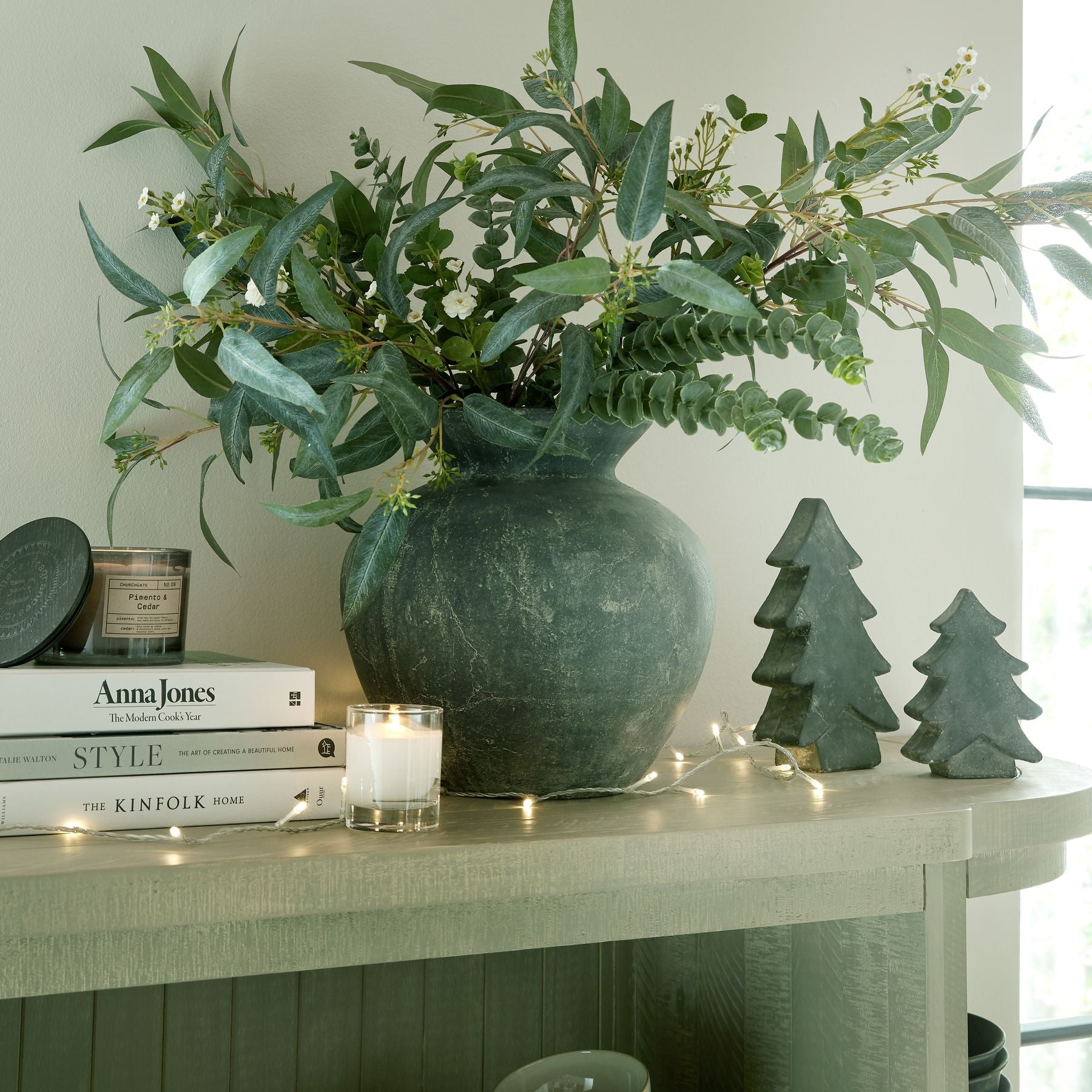 Decorative setup with a vase of greenery, books, and small trees on a surface.
