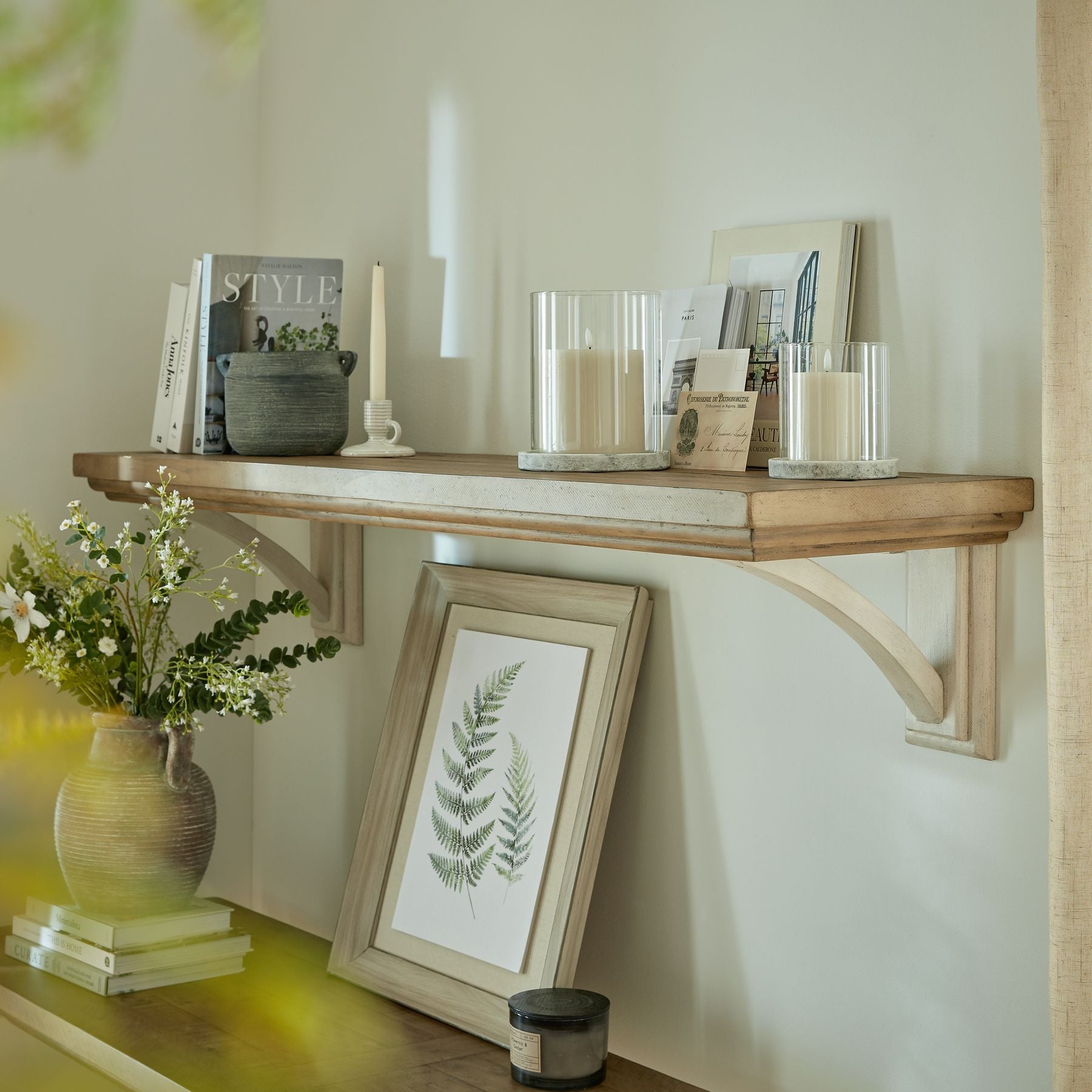 Wooden shelf with decorative items including books, candles, and a framed picture in a home setting.