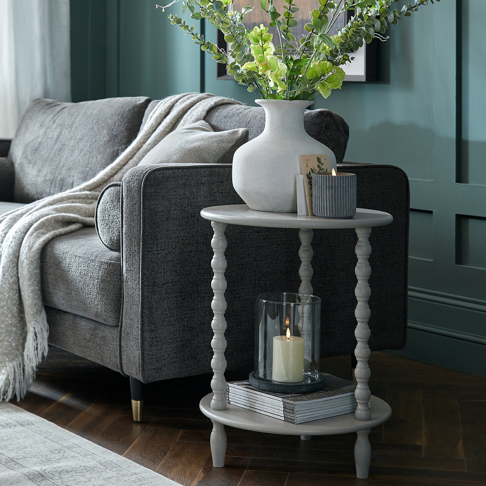 Gray sofa with a white side table featuring a candle and vase, against a teal wall.