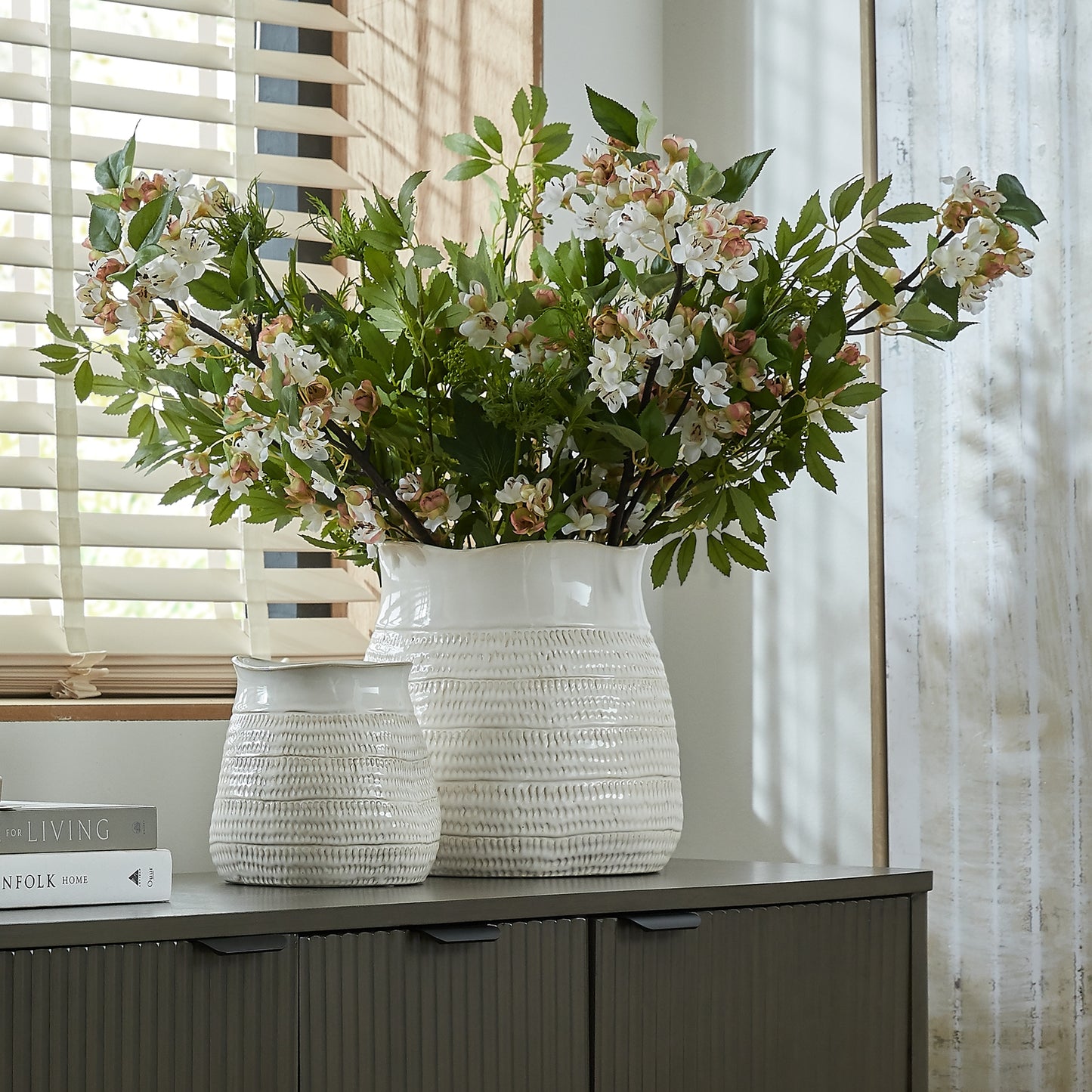 White textured vase with flowers on a cabinet against a window background