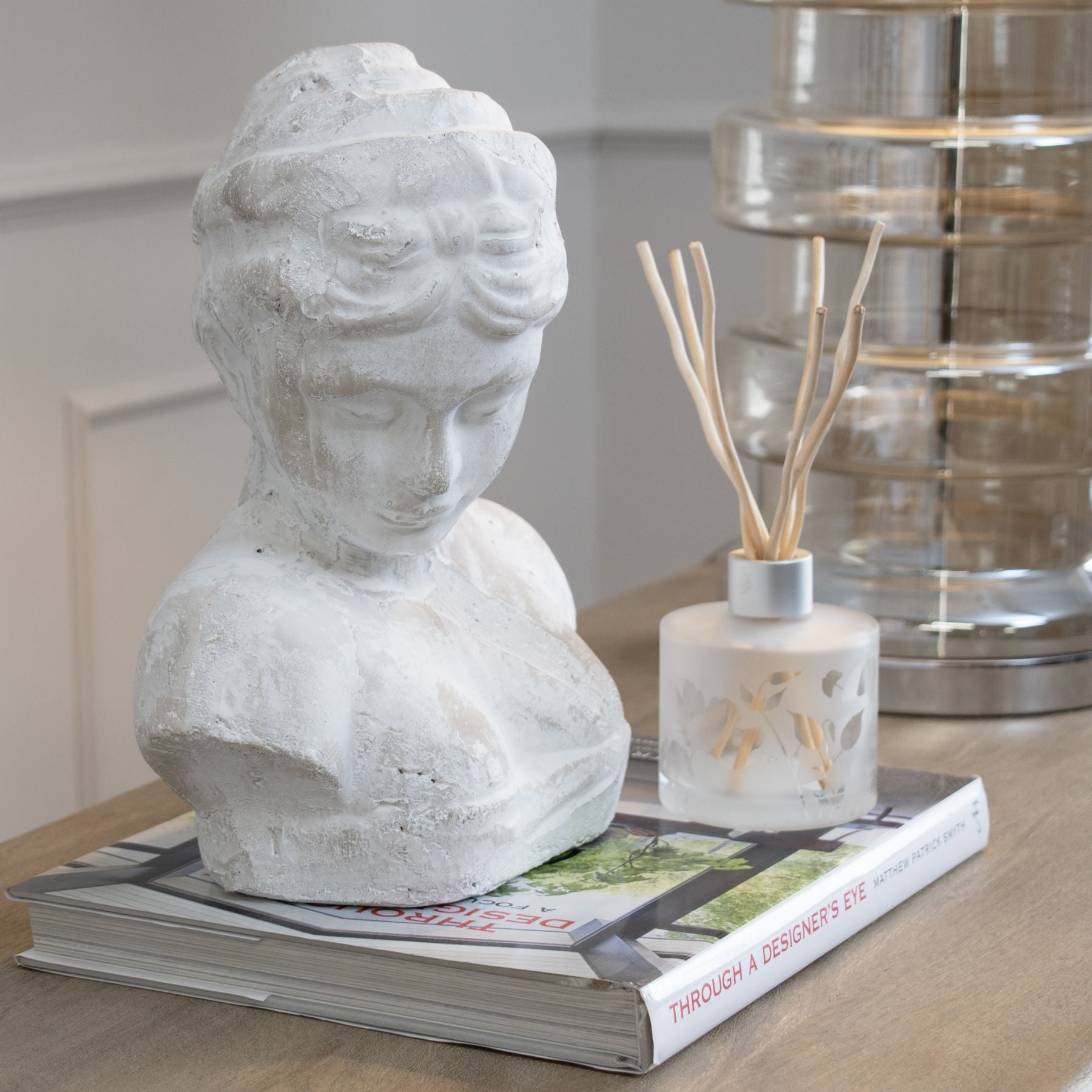 Decorative bust on a book with a diffuser bottle and glass container in the background
