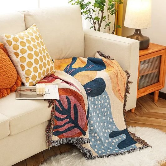 Colorful abstract-patterned throw blanket draped over a beige sofa with decorative pillows.