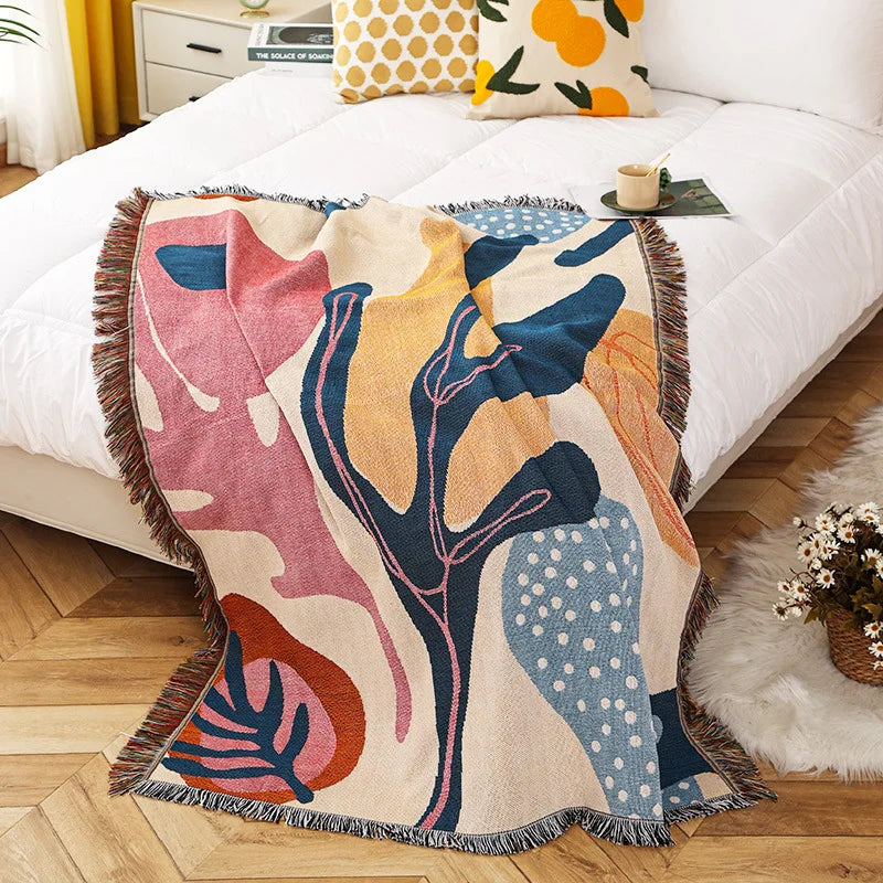 Colorful abstract-patterned throw blanket on a bed with decorative pillows and a small table.