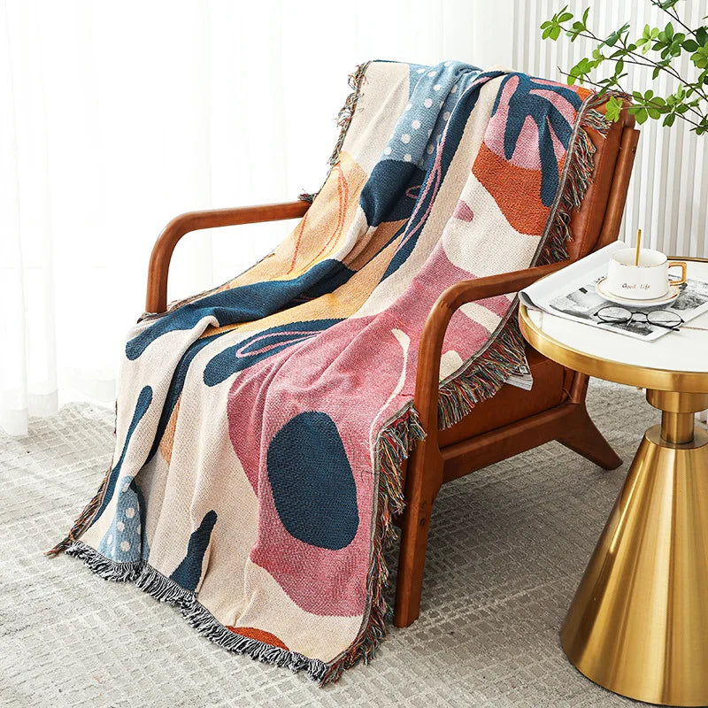 Colorful abstract patterned blanket draped over a wooden chair in a cozy room.