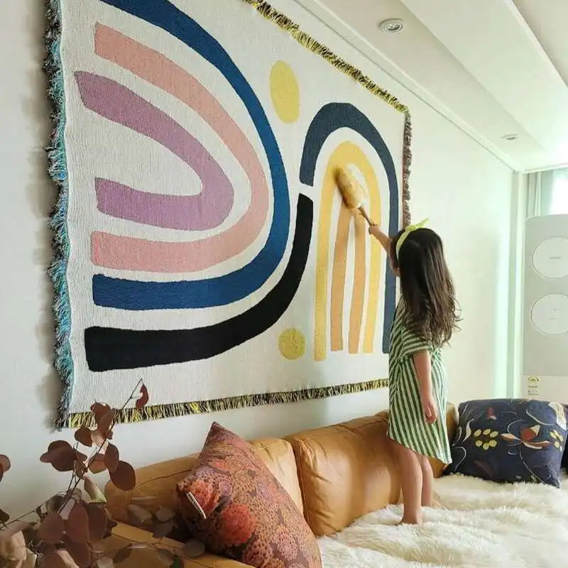 Child painting a colorful abstract wall hanging in a room with a couch and pillows.