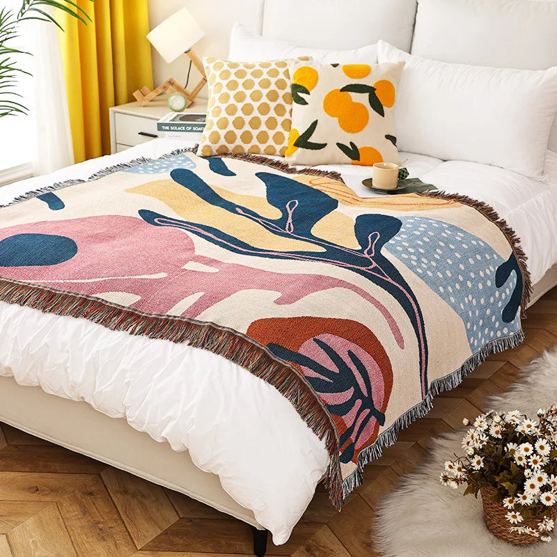 Colorful abstract-patterned throw blanket on a bed with pillows and a cup.