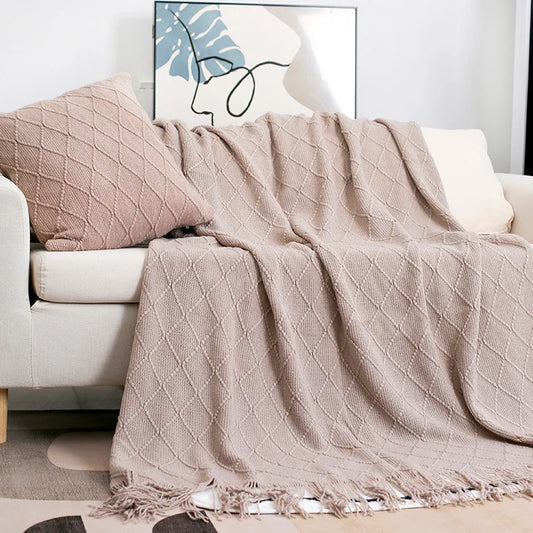 Beige textured throw blanket draped over a white sofa with a pillow in a living room setting.