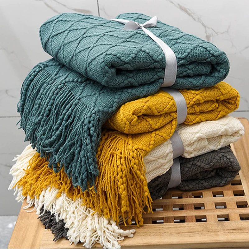 Stack of colorful textured blankets on a wooden surface with a light gray background